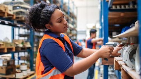 Woman wearing a hi-vis jacket scanning items in a warehouse