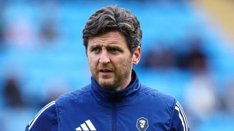 Alex Bruce holding a football under his right arm against a blurred background of blue seats