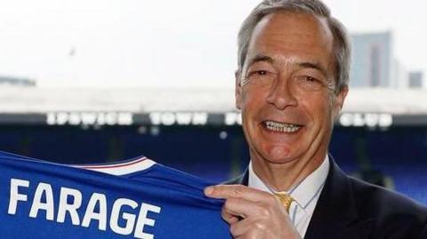 Nigel Farage holding a football shirt.