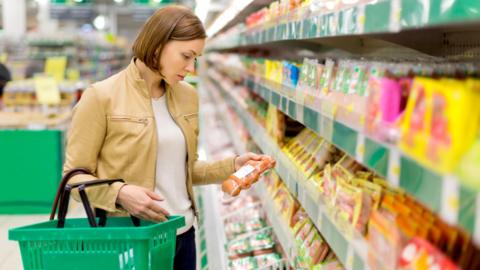 A woman looks at sausages in a supermarket - stock shot