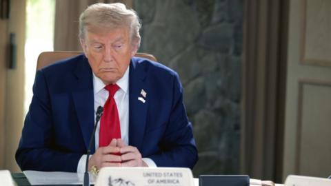 Donald Trump at G7 meeting in Alberta, sat at a table, hands clasped, looking to the right