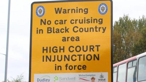 A large yellow sign with a black border. In black writing it states: Warning - no car cruising in Black Country area - High Court Injunction in force.