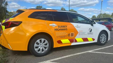 An orange and white care with "Surrey Highways" on the side along with "Surrey County Council" and its logo.