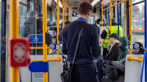 A tram conductor in a navy blue uniform with short dark hair is collecting fares from passengers