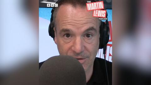 Martin Lewis wearing headphones sitting in a studio behind a black microphone