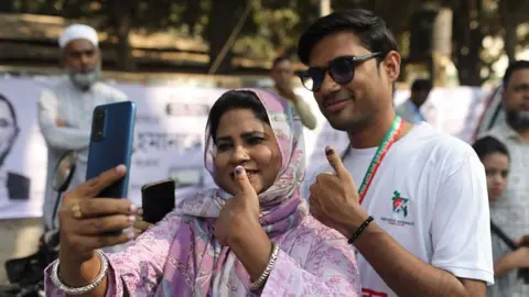 A man and woman in Bangladesh take a selfie while showing off their marked thumbnails