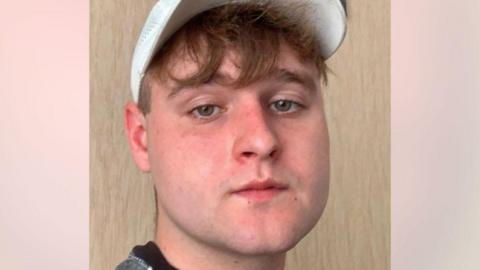 Curtis Ross, a young man looking at the camera, he is wearing a white baseball cap.
