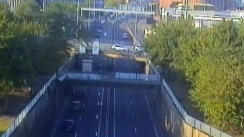 A traffic camera view of a dual carriageway with a long line of stationary traffic