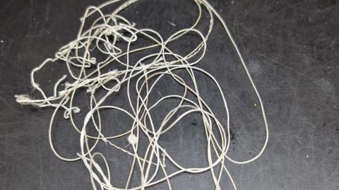 A white length of string tangled up on a table with a black surface.  