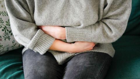 Woman sat on sofa with arms wrapped around her middle