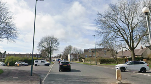 A Google Streeview image of a junction showing a main road with two side roads coming off it. The image contains a number of vehicles coming out from the side roads and traffic heading away from the camera.