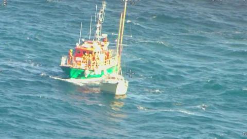 A coastguard boat approaches a white yacht bobbing on the sea during a rescue operation.