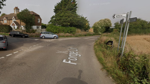 A Google Map image of the road into Lidsing, on the outskirts of Maidstone, Kent. There are three cars to the left and a field to the right. 