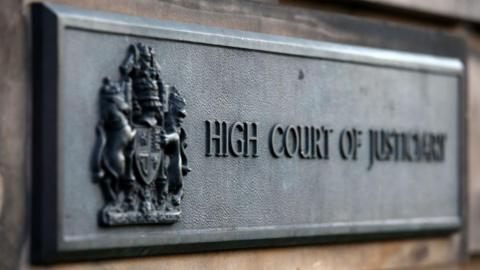 A metal sign outside a court building reading 'High Court of Justiciary'