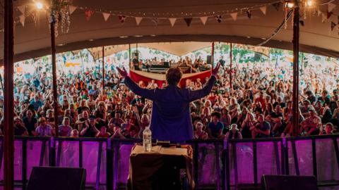 Person stood on stage performing to audience in tent