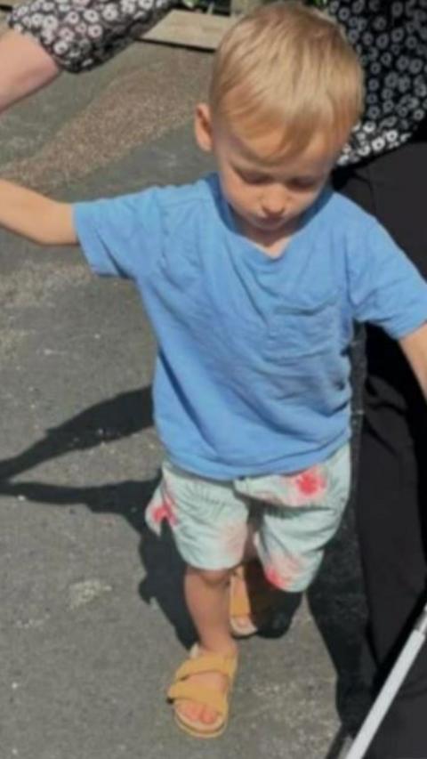 A boy wearing a light blue t-shirt walking.