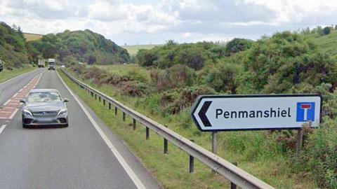 a car on a road beside a bushy grass verge and a road sign pointed to Penmanshiel