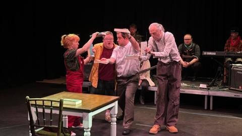 Four people performing on a stage with musicians in the background