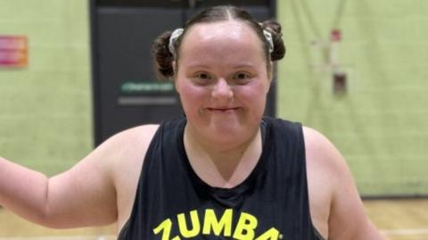 Hannah, who has brown hair tied into two bunches and is wearing a black vest, smiles at the camera