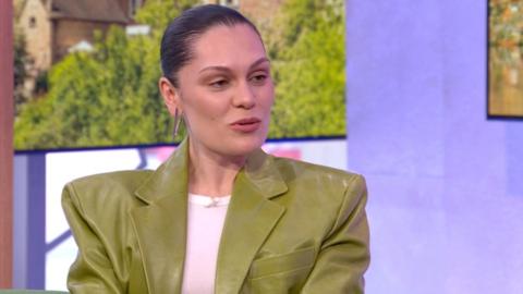 Jessie J is wearing a green leather jacket with wide shoulders. Her hair is slicked back.