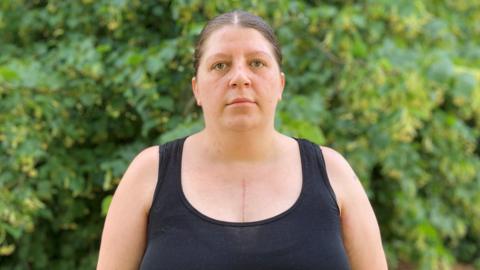 A woman in a black top with her hair tied back looks at the camera.