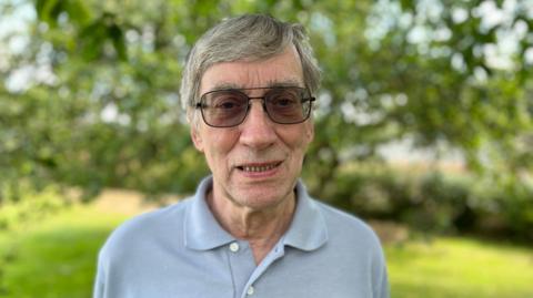 Phil Emmett, a man with grey hair wearing sunglasses, in his garden