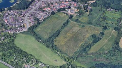 An aerial view of the proposed development site, consisting of two fields on the edge of a older housing area