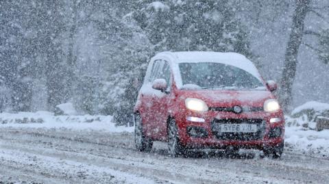 A car drives through the snow in Aviemore in the Highlands