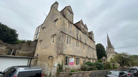 Three story Cotswold stone apartment block with church in background