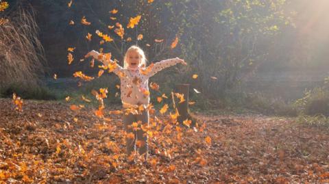 A photo of a girl playing in colourful autumn leaves