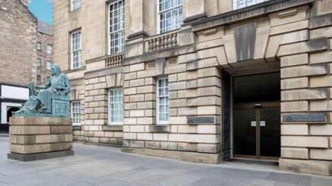 The outside of the High Court in Edinburgh building. It has sandstone coloured pricks and a statue at the front.