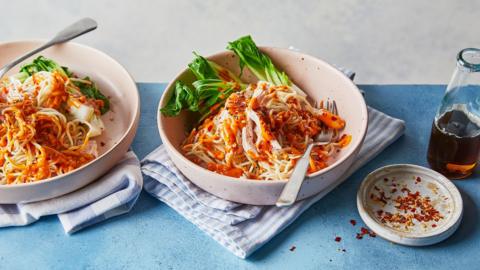 Light coloured bowl on a blue-striped napkin with noodles and veg in it
