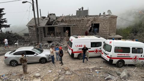 Lebanese Red Cross vehicles parked outside a building hit by an Israeli strike, surrounded by debris.