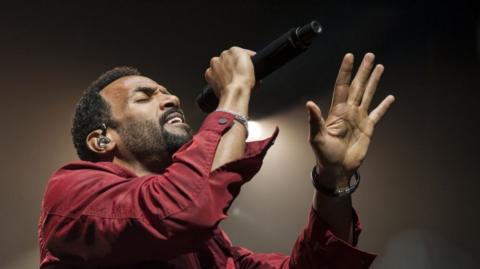 Craig David singing and holding up five fingers