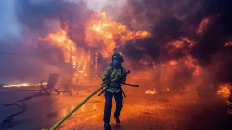 A firefighter battles the Palisades Fire as it burns during a windstorm on the west side of Los Angeles, California,