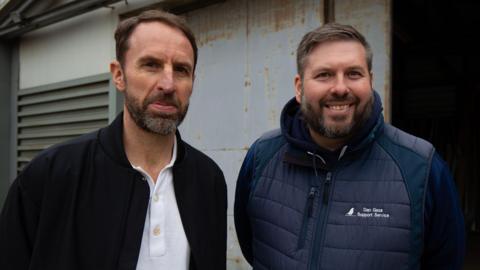 Gareth Southgate is posing for a photo with another man who is smiling. Both men have short brown hair and beards.