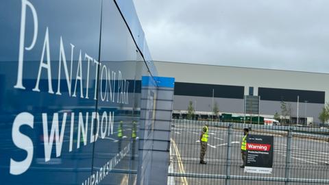 A sign which says 'Panattoni Park' and two people in camo outfits outside an industrial building.