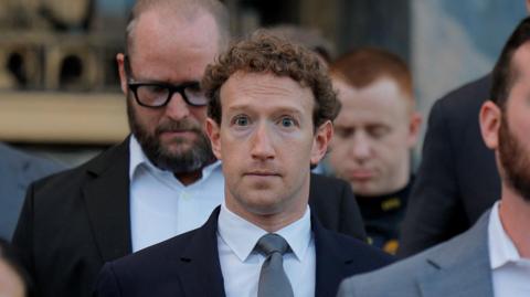 Mark Zuckerberg walking down the grey stone steps of a Los Angeles court house wearing a navy suit blazer, grey neck tie and white shirt. 
