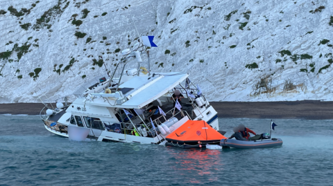 The Channel Queen partially submerged, relatively close to the shore, with white cliffs in the background 