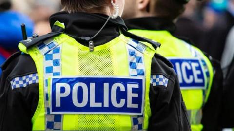 The back of two police officers wearing high-vis vests with the word POLICE on the back