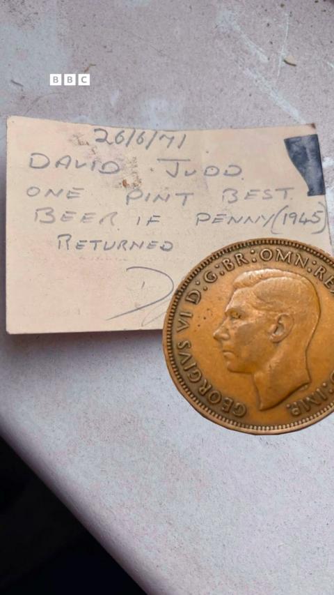 An old penny on top of a piece of card - on it is written: David Judd - one pint of best beer if penny returned