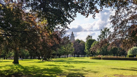 A picture of a lawn at the War Memorial Park lined with trees and with a war memorial in the background