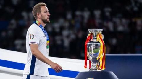 Harry Kane walks past the trophy