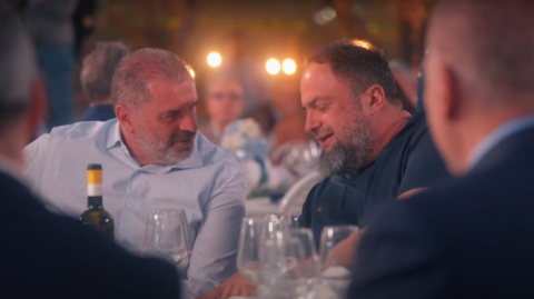 Ange Postecoglou (left) and Evangelos Marinakis (right) sit next to each other at dinner