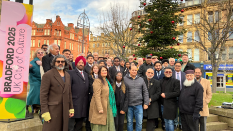 A large group of people gathered together in Centenary Square in Bradford with a green Christmas Tree to the right of the image