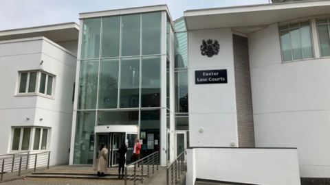 Exterior of Exeter Law Courts featuring modern architecture with large glass panels and white walls. Three people are near the entrance, with one entering the building.