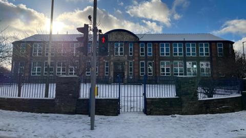 The front of St Ninian's High School, which is a long brown, brick building with lots of windows, with the the car park covered in snow and the gate closed.