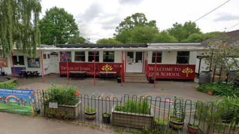 The entrance to Tipton St John Primary School, a white and red building with a sign saying 'welcome to our school'