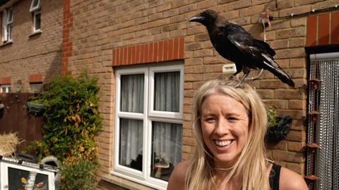 Crow sits on the head of a woman. The woman is smiling.