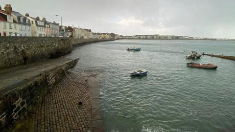 A sea wall and boats moored at low tide on a cloudy day